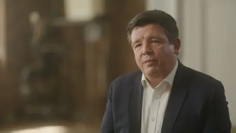 Neil Jefferson, a man with short brown hair, in a white shirt and blazer