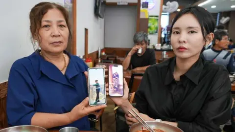 BBC/Hosu Lee Two women, one older, one younger, sit in a cafe holding phones with images of an older man.