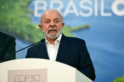 getty President Lula in white shirt and dark blue suit jacket with a backdrop of a poster of the Amazon and the COP30 logo